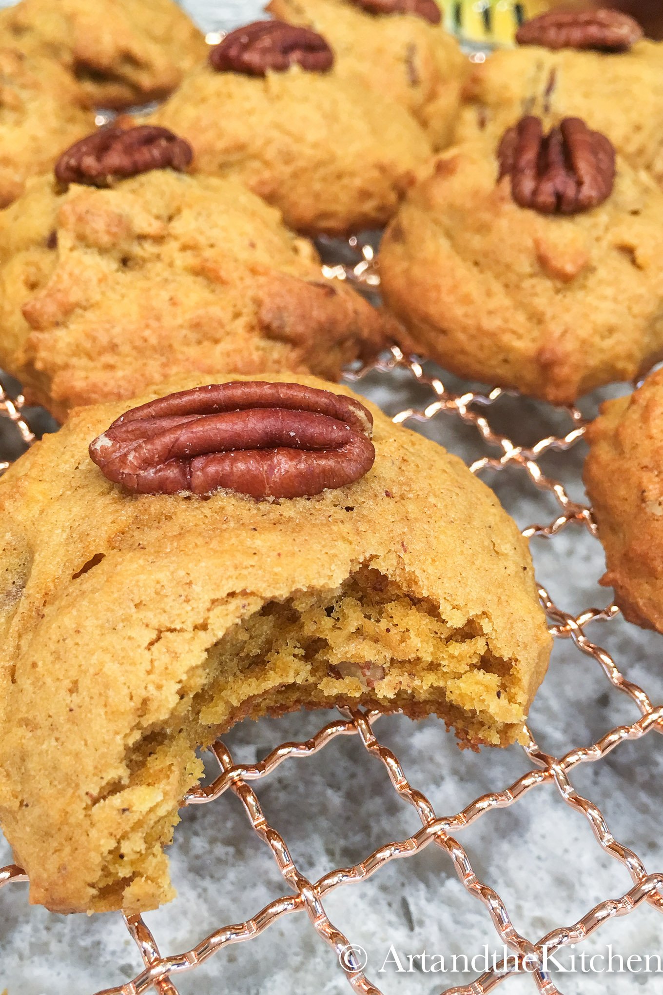 Wire rack filled with pumpkin cookies topped with a pecan. One cookie with bite out of it.