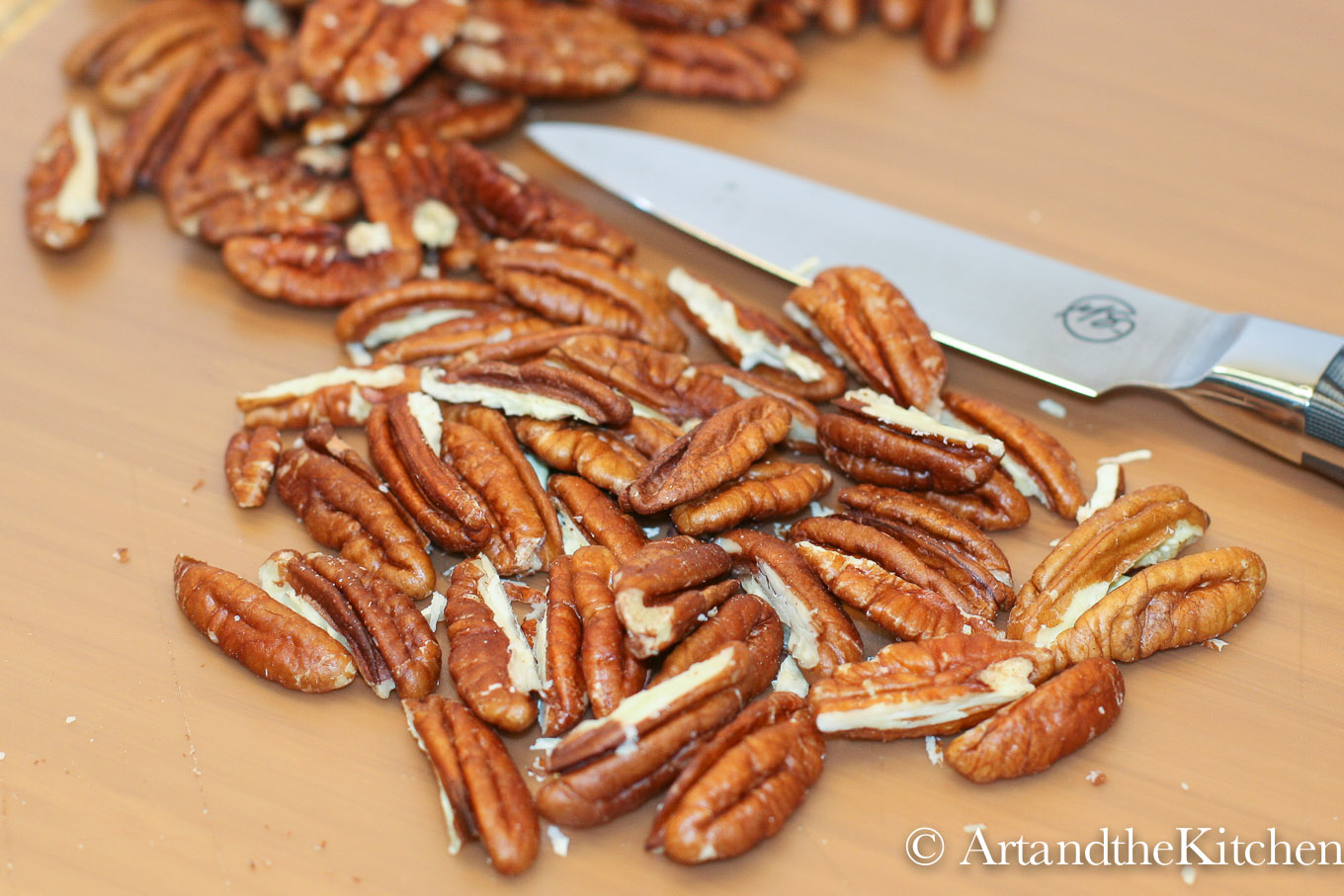 Cutting board with chopped pecans and stainless steel knife.