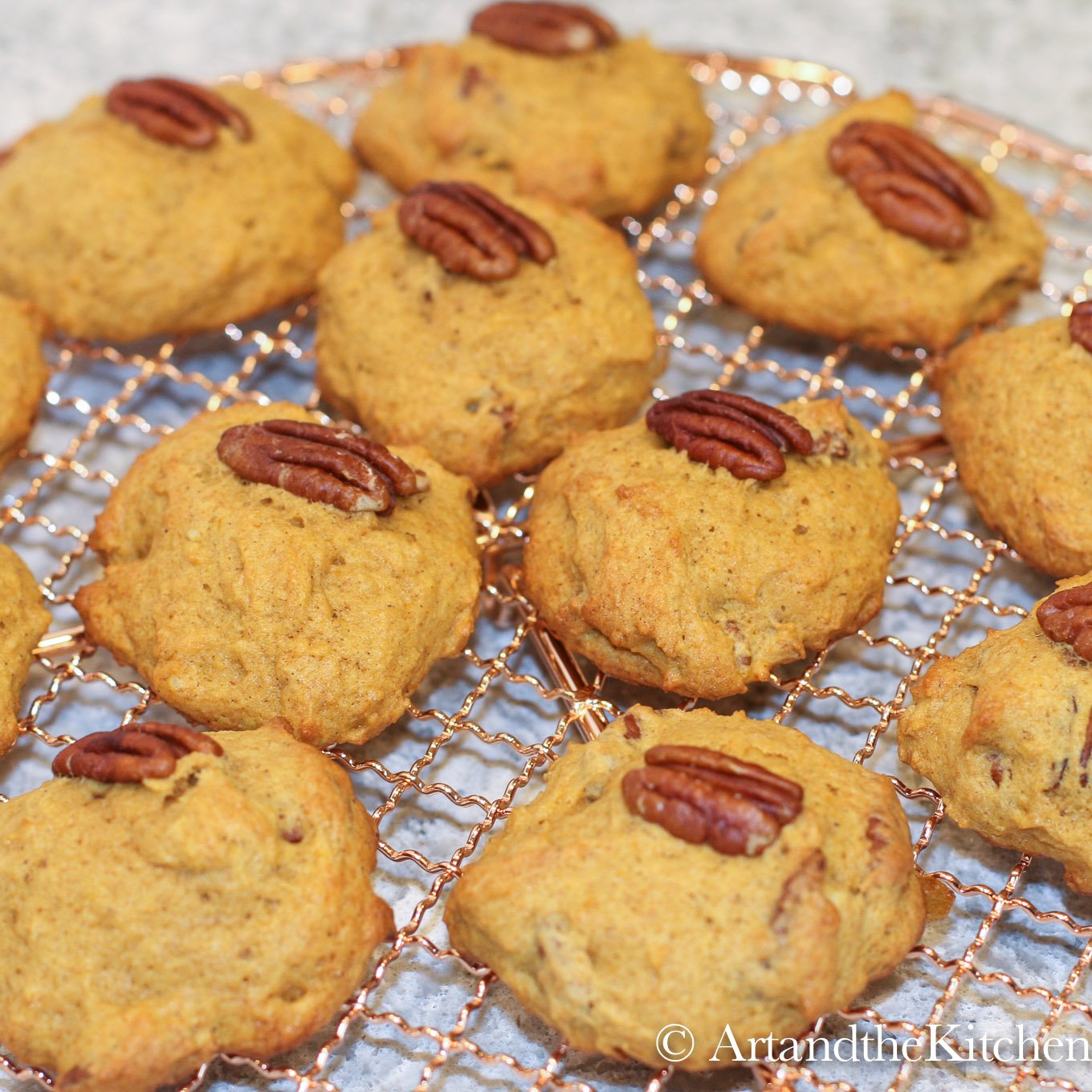 Copper wire rack filled with pumpkin cookies topped with a pecan.