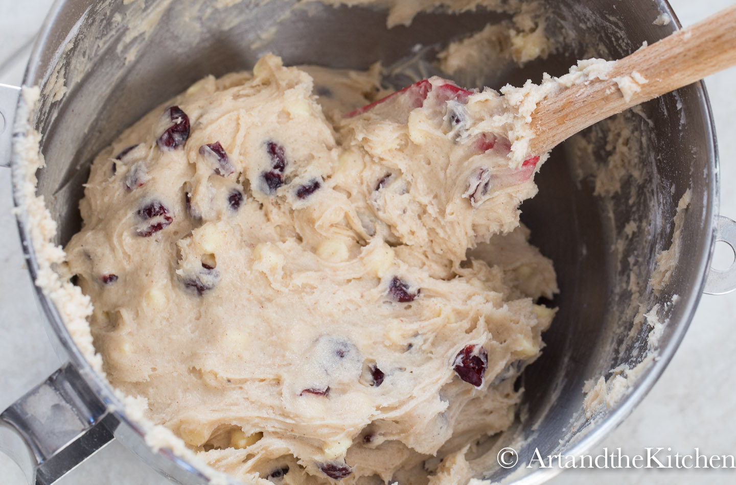 Stainless steel mixing bowl filled with cookie dough with cranberries in it.