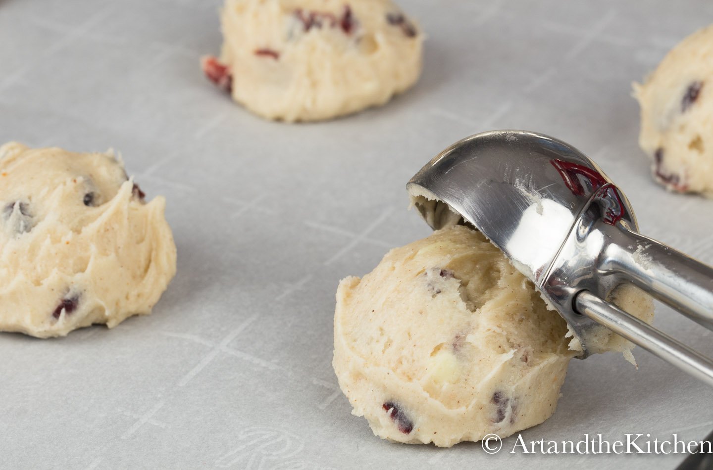 Cookie scoop placing scoopful of dough on white parchment lined baking sheet.