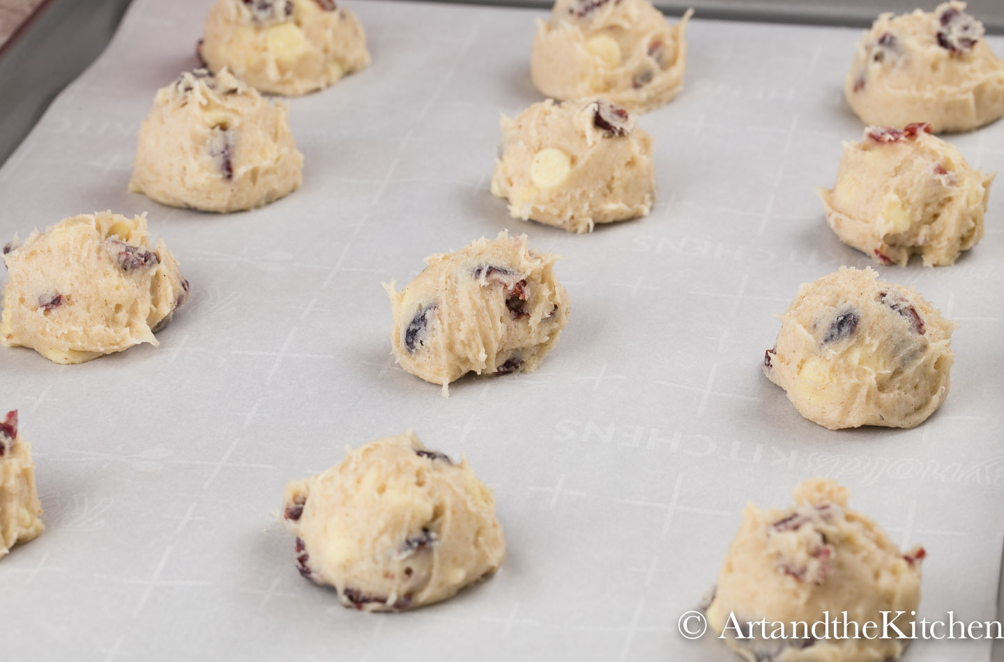 Scoops of cookie dough on white parchment lined baking sheet.