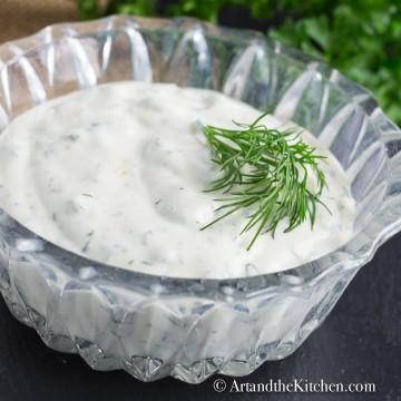 Glass bowl filled with ranch dip, garnished with dill sprig.