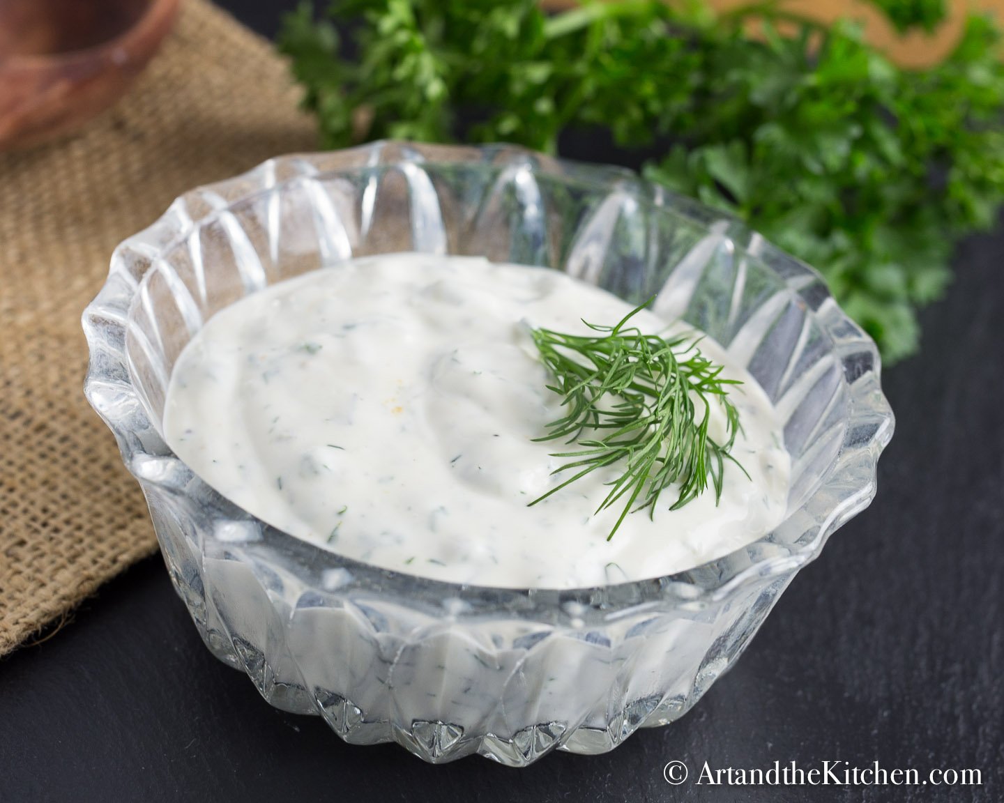 Glass bowl filled with ranch dip, garnished with dill sprig.