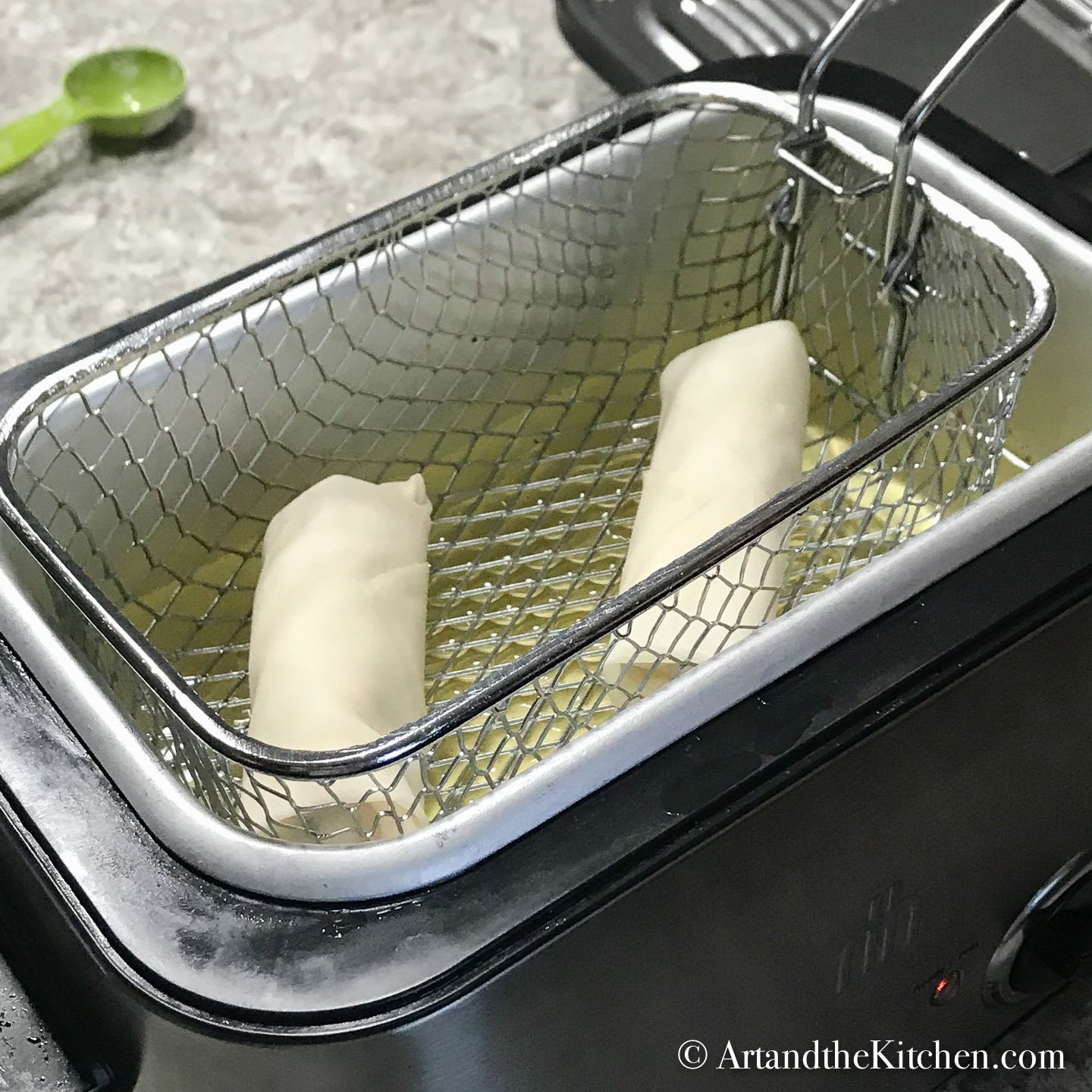 Two spring rolls in basket of deep fryer.