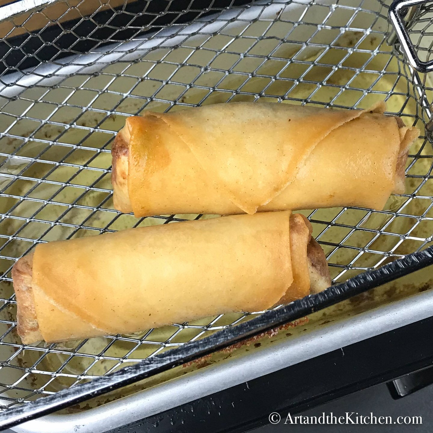 Two spring rolls in basket of deep fryer.