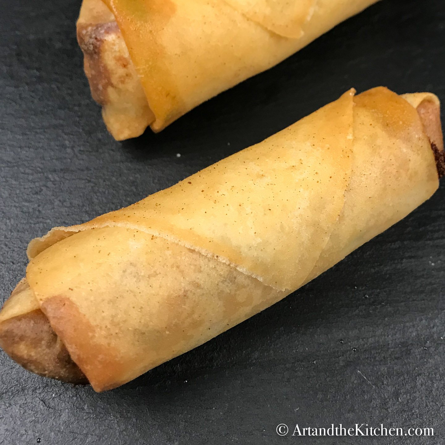 Two fried spring rolls on black slate cutting board.