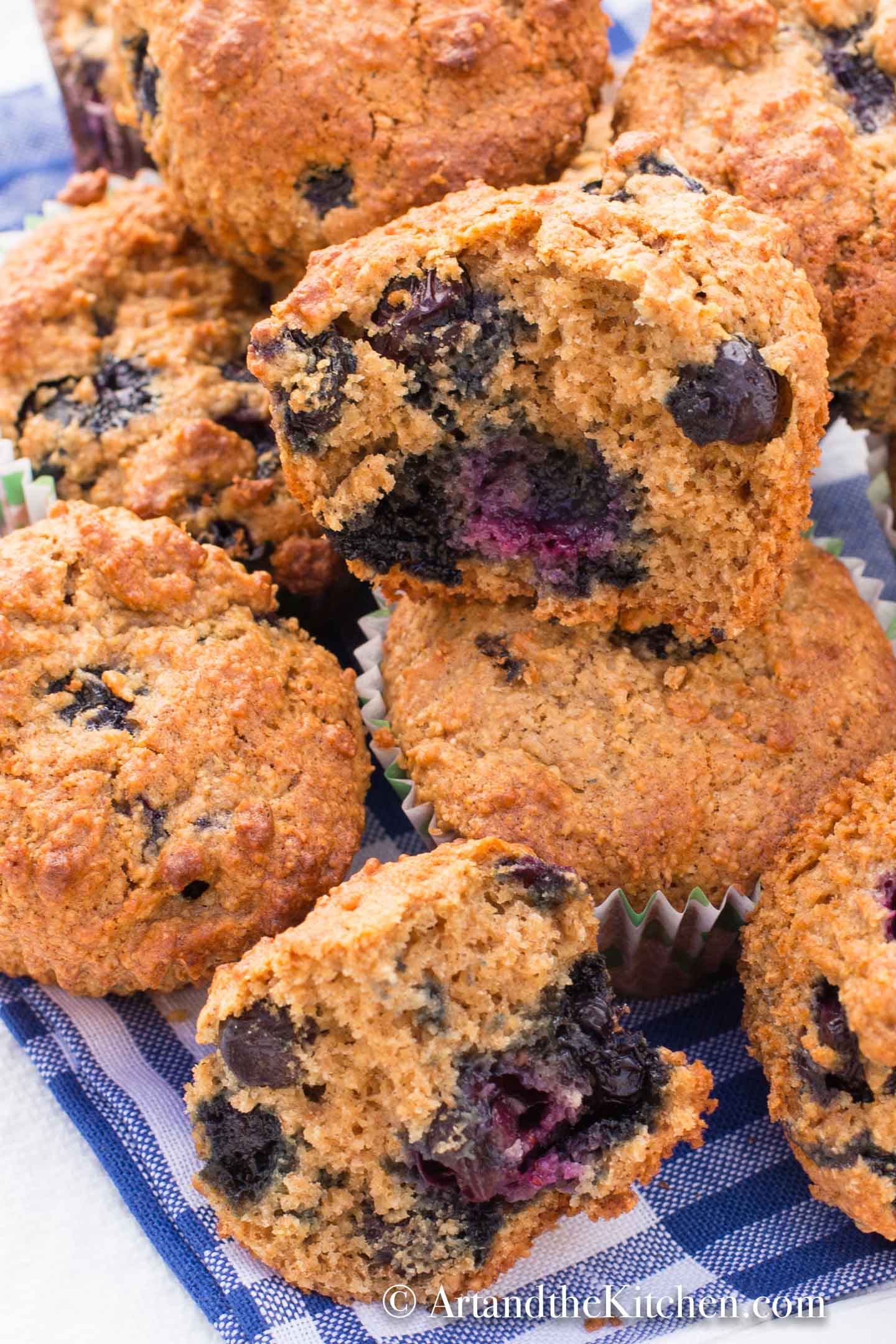 Bran muffins loaded with blueberries on gingham tablecloth.