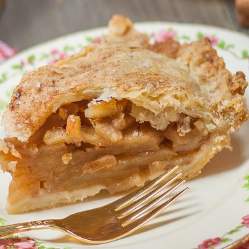 Slice of apple pie on decorative plate with gold plated fork.