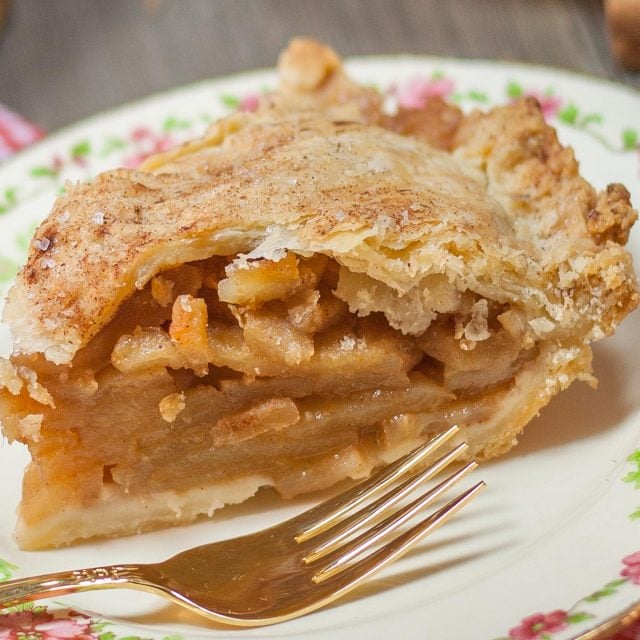 Slice of apple pie on decorative plate with gold plated fork.