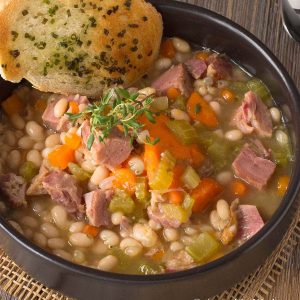 Bowl of ham and bean soup garnished with slice of garlic toast.