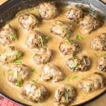 Meatballs simmering in a creamy sauce in a cast iron skillet, garnished with chives.