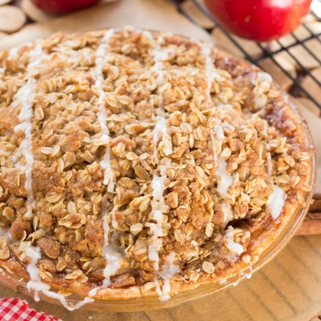 Apple pie in a glass pie plate with a crunchy oatmeal top, drizzled with icing.