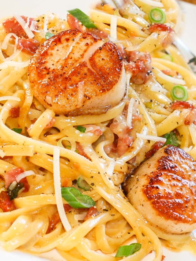 Creamy linguine pasta with two seared scallops, garnished with green onions, shredded parmesan cheese and pepper.