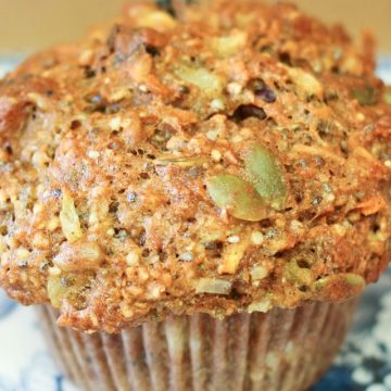 Muffin loaded with seeds, dried fruit, carrots and more on decorative blue plate.