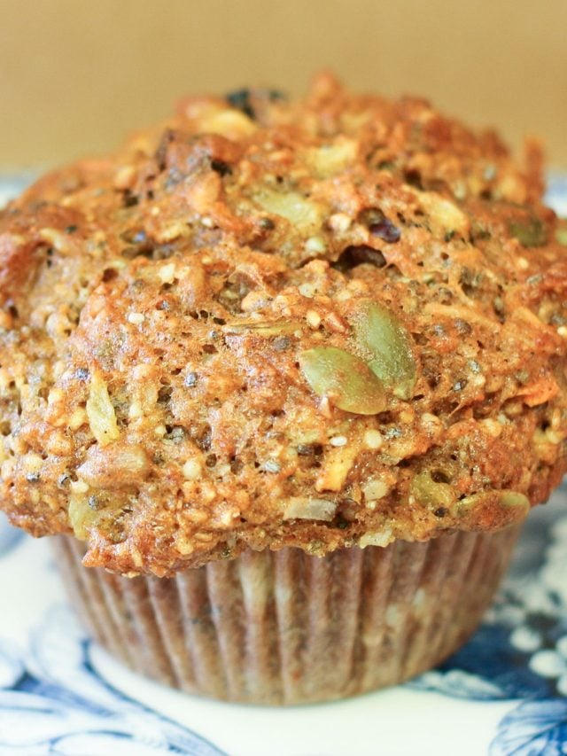 Muffin loaded with seeds, dried fruit, carrots and more on decorative blue plate.