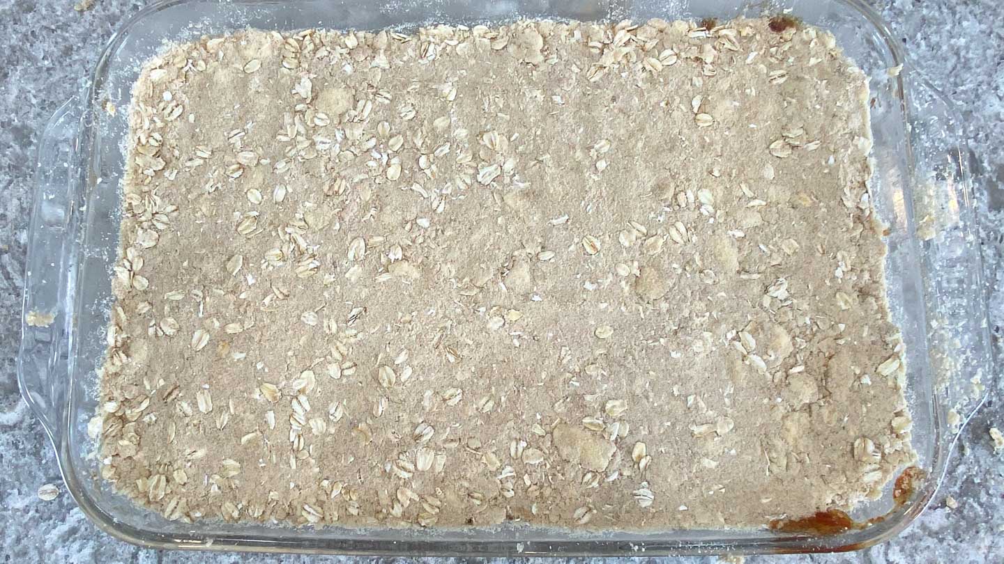 Oatmeal crumb mix on top of cooked dates in glass baking pan.