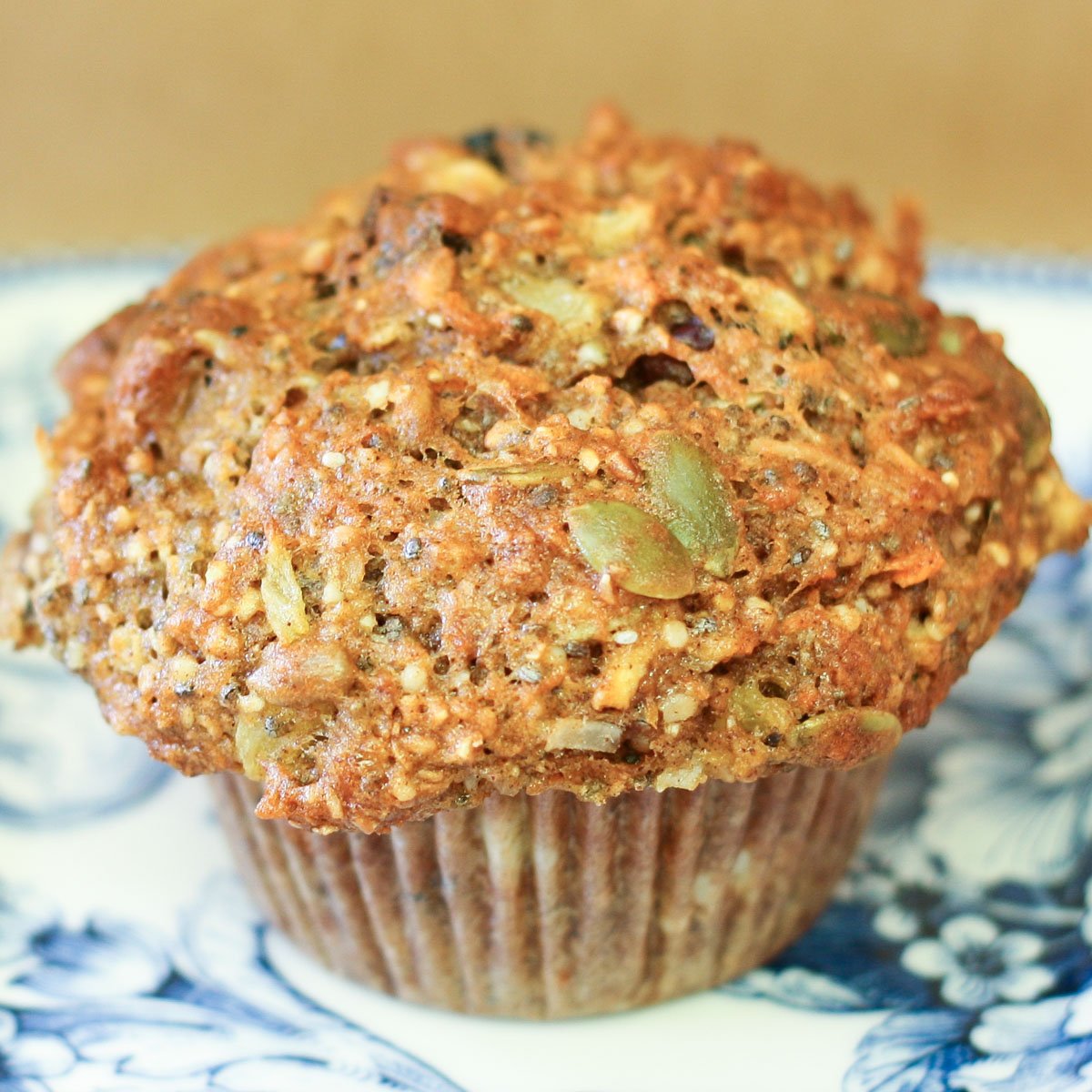 Muffin loaded with seeds, dried fruit, carrots and more on decorative blue plate.