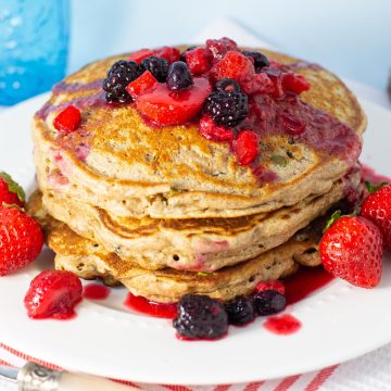 Stack of whole wheat pancakes topped with berries on white plate