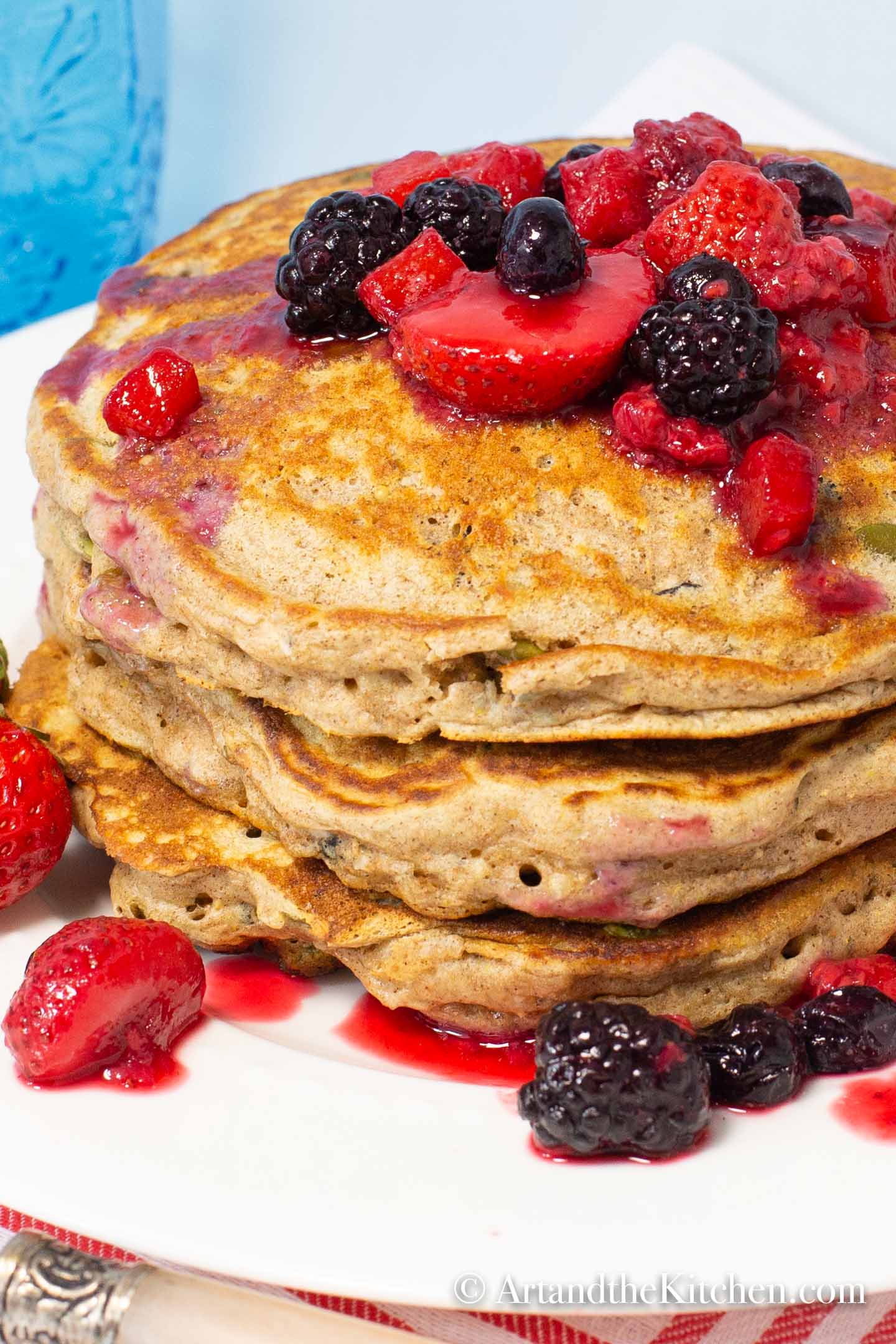 Stack of whole wheat pancakes topped with berries on white plate
