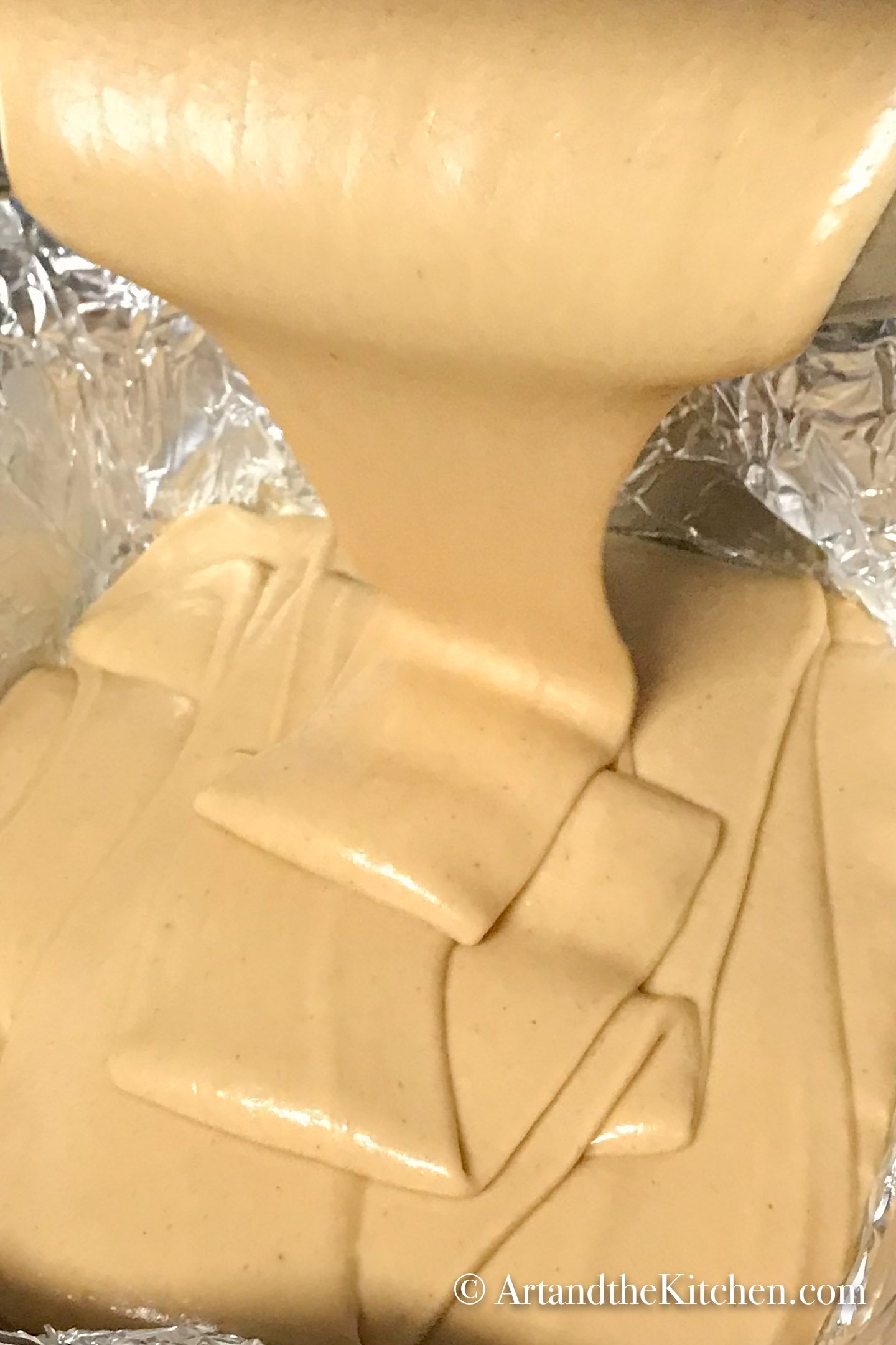 Peanut butter fudge being poured into foil lined baking pan.