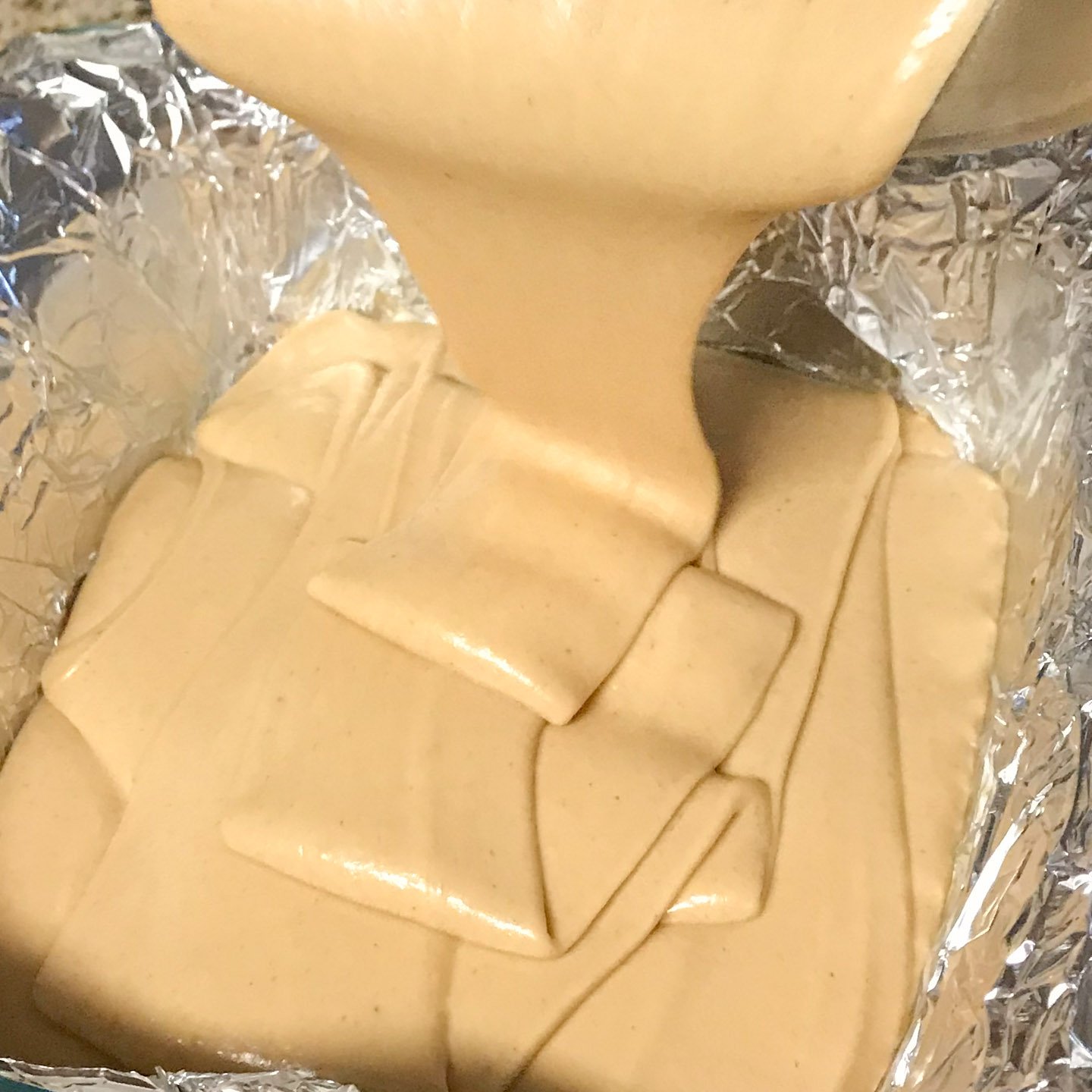 Peanut butter fudge being poured into foil lined baking pan.