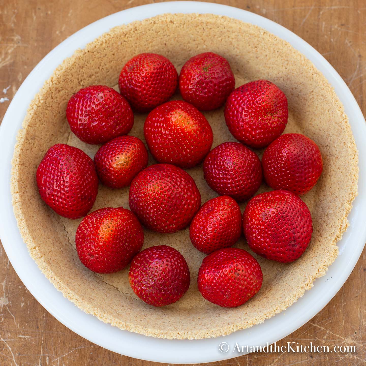 White pie plate filled with a graham cracker crust and fresh whole strawberries.