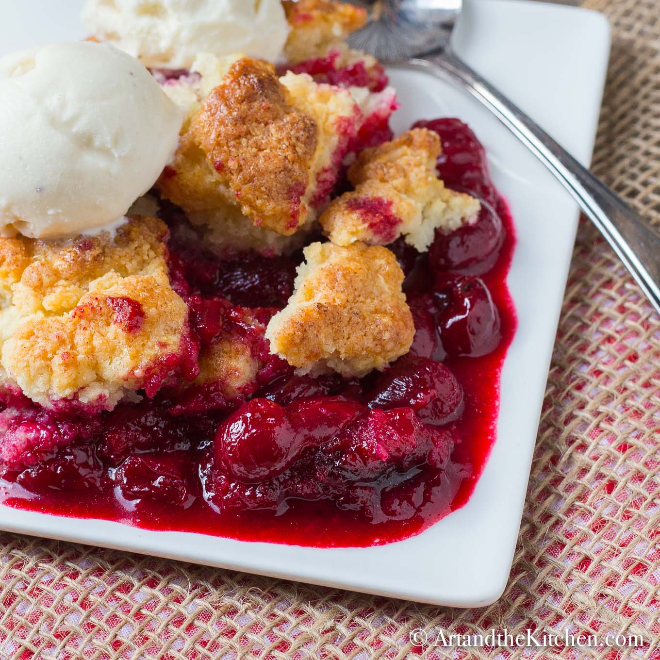White plate filled with cherry cobbler, topped with scoop of ice cream.