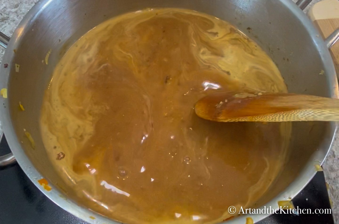 Brown gravy in stainless steel pot with wood spoon.