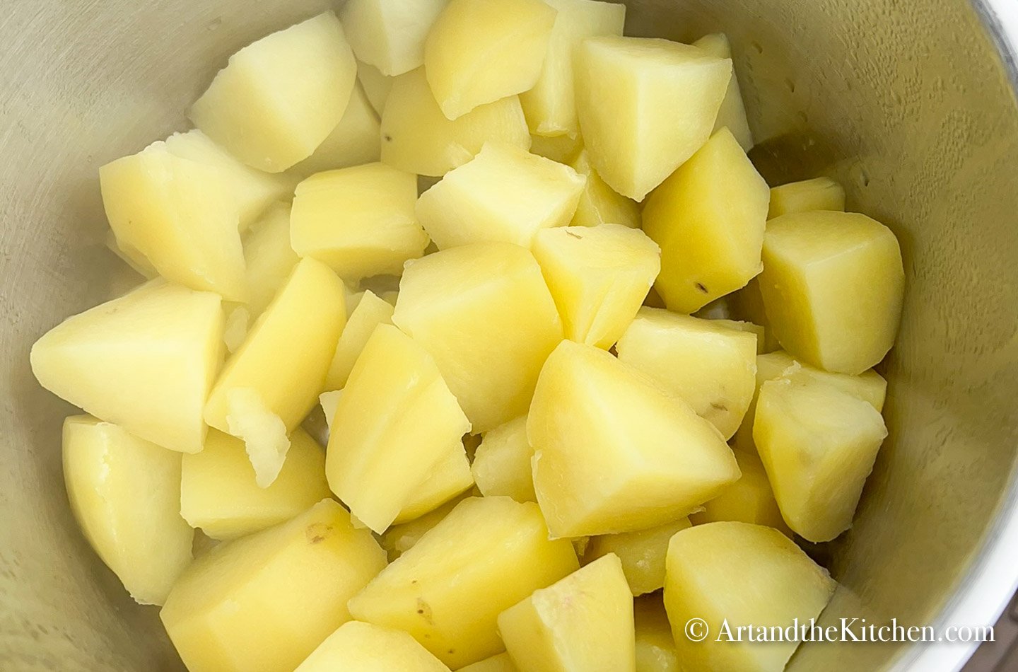 Stainless steel pot of cooked cubed potatoes.
