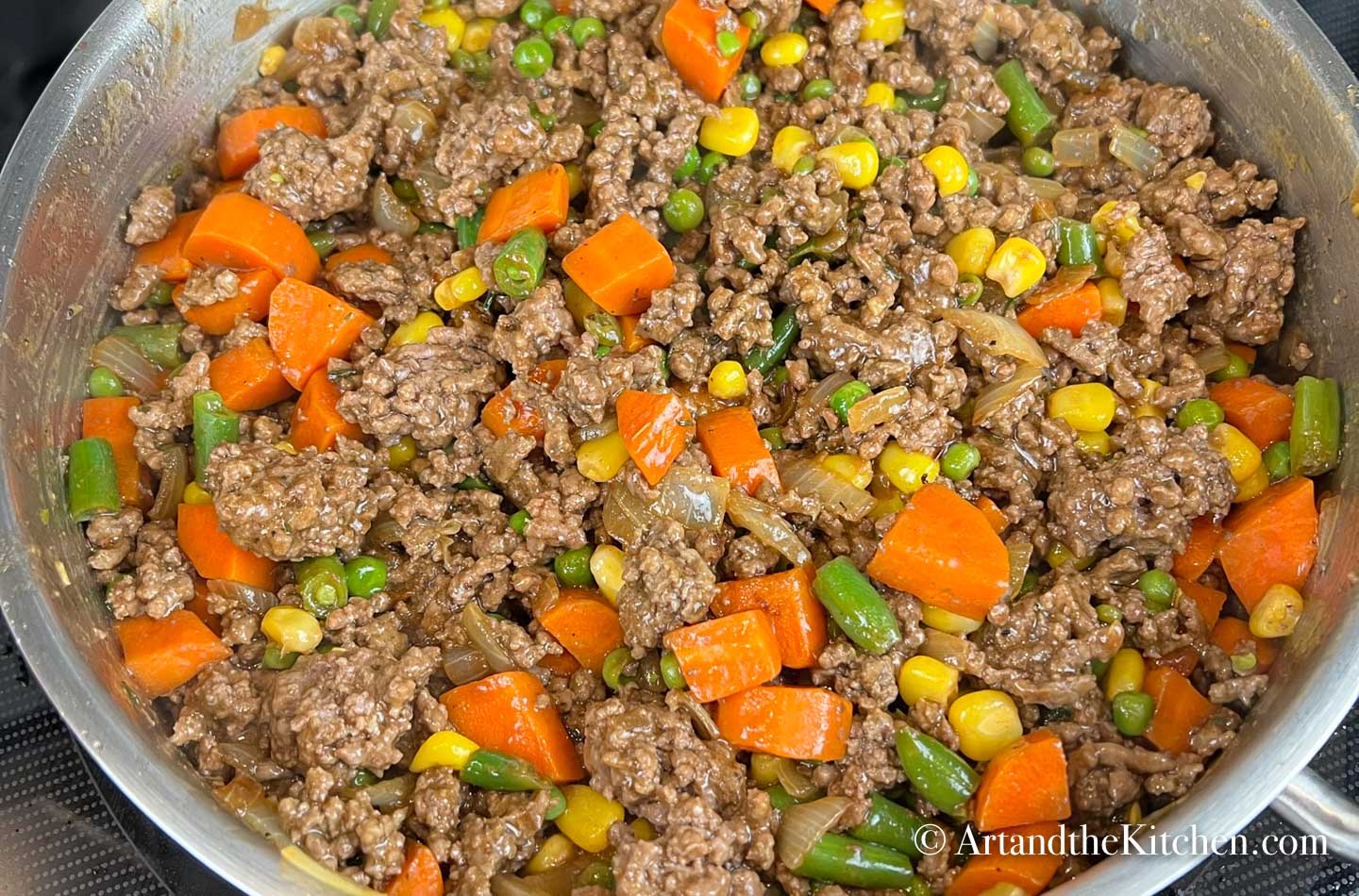 Stainless steel skillet filled with cooked ground beef and vegetables in gravy.