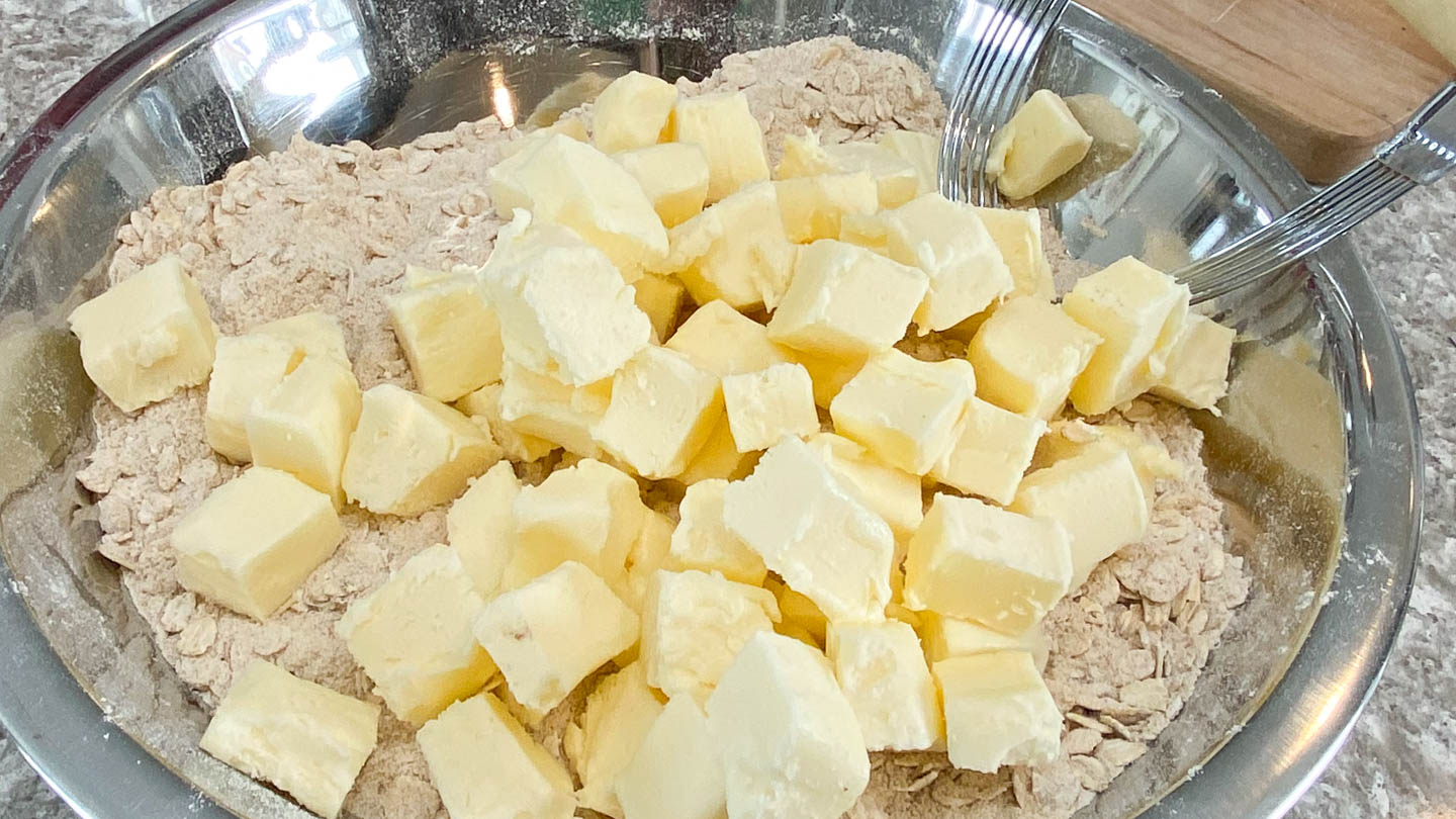 Cubes of butter on top of dry baking ingredients in stainless steel bowl.