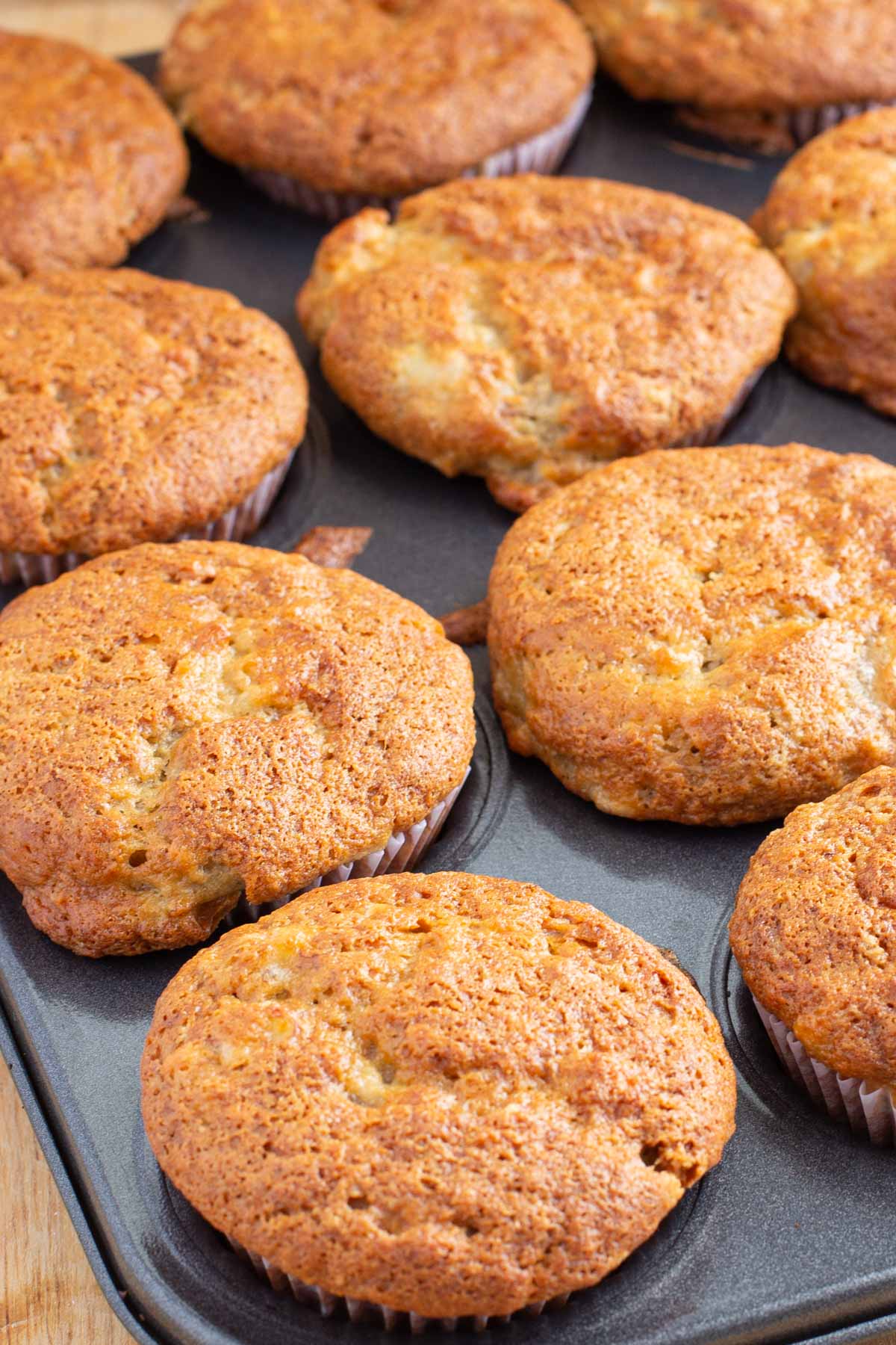 Muffin tin full of banana muffins with golden brown crisp tops.