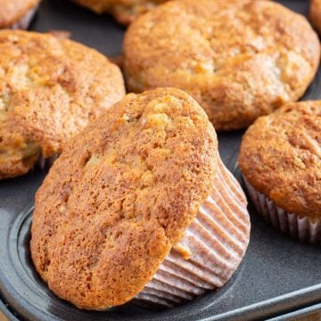 Muffin tin full of banana muffins with golden brown crisp tops.