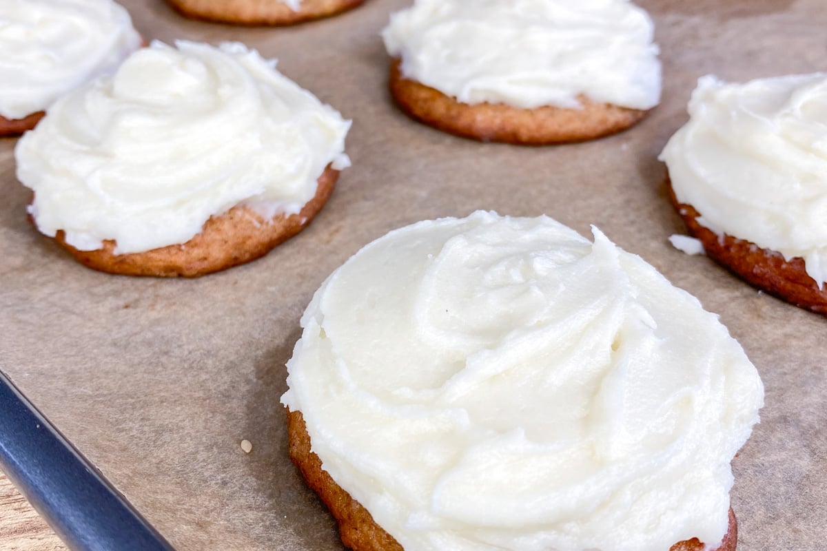 Fluffy banana cookies with frosting on brown parchment lined baking sheet.