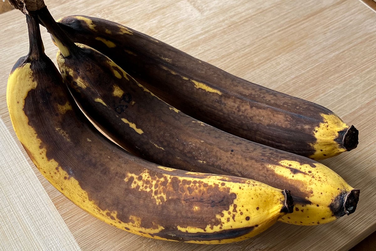 Bunch of overripe bananas on wood board.