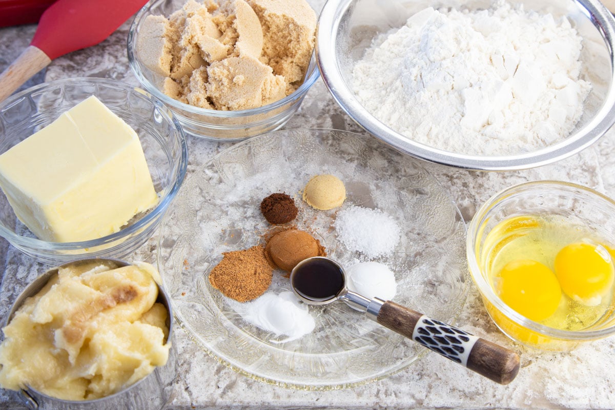 Ingredients of spices, flour, eggs, butter, brown sugar and bananas in bowls.