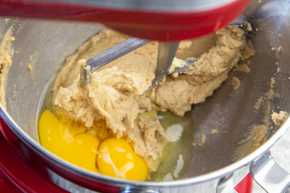 Two eggs added to cookie dough in stainless steel mixing bowl with paddle attachment.