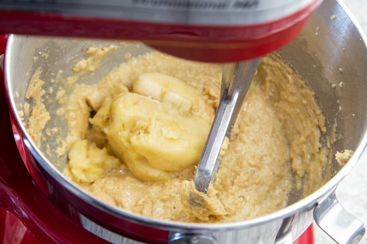 Mashed bananas added to cookie dough in stainless steel mixing bowl with paddle attachment.