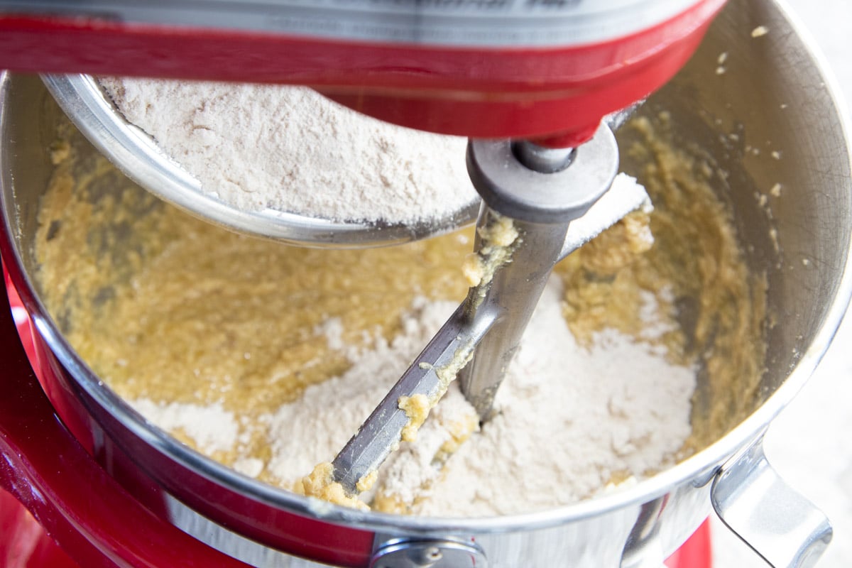 Flour added to cookie dough in stainless steel mixing bowl with paddle attachment.