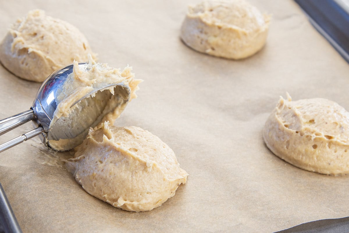 Scoops of banana cookie dough on brown parchment lined baking sheet.