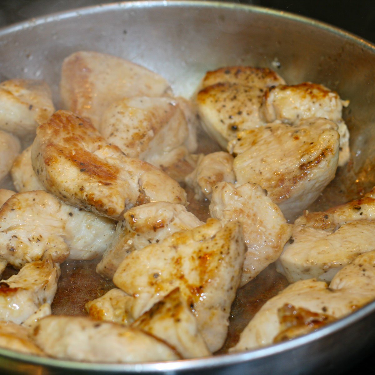 Chopped chicken frying in stainless steel frying pan.