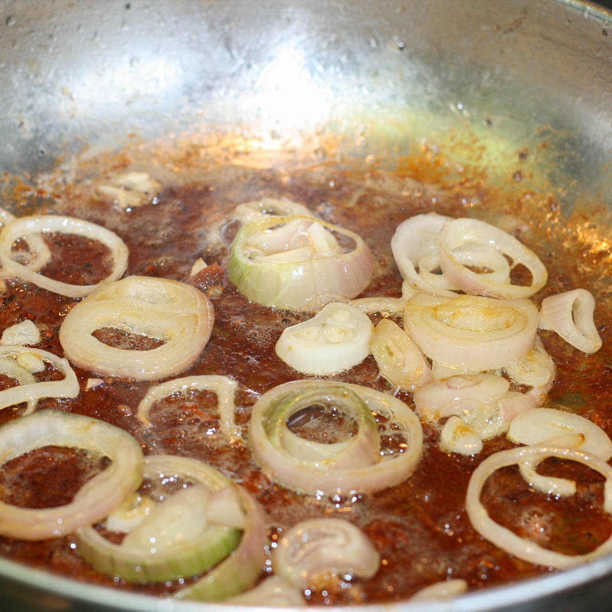 Sliced shallots sautéing in frying pan with browned bits from searing chicken.