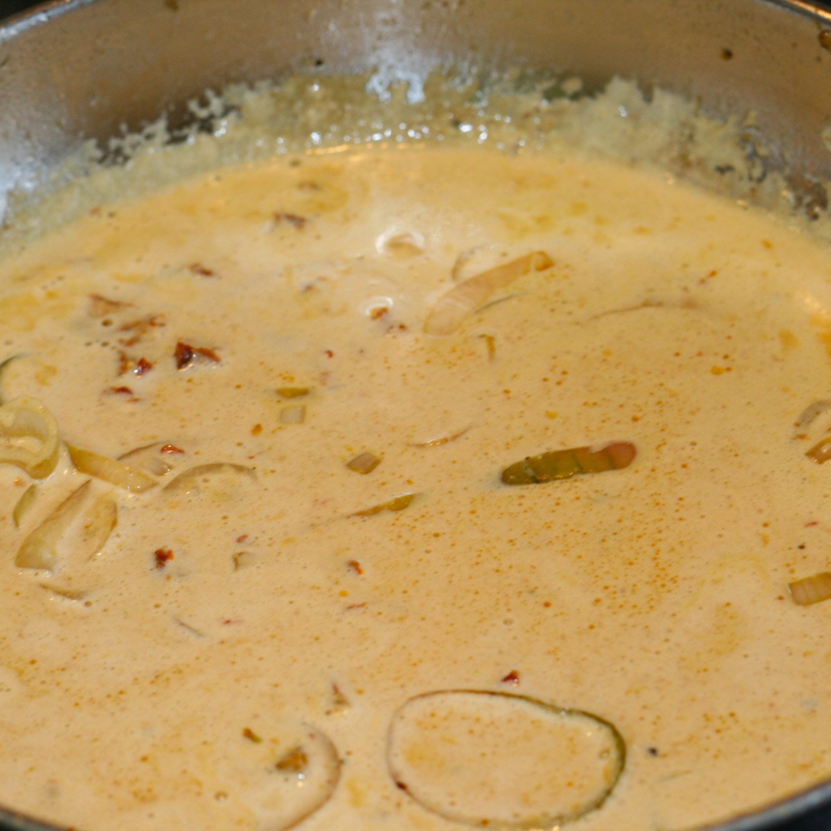 Sauce of sun-dried tomatoes, shallots, white wine and cream simmering in skillet.