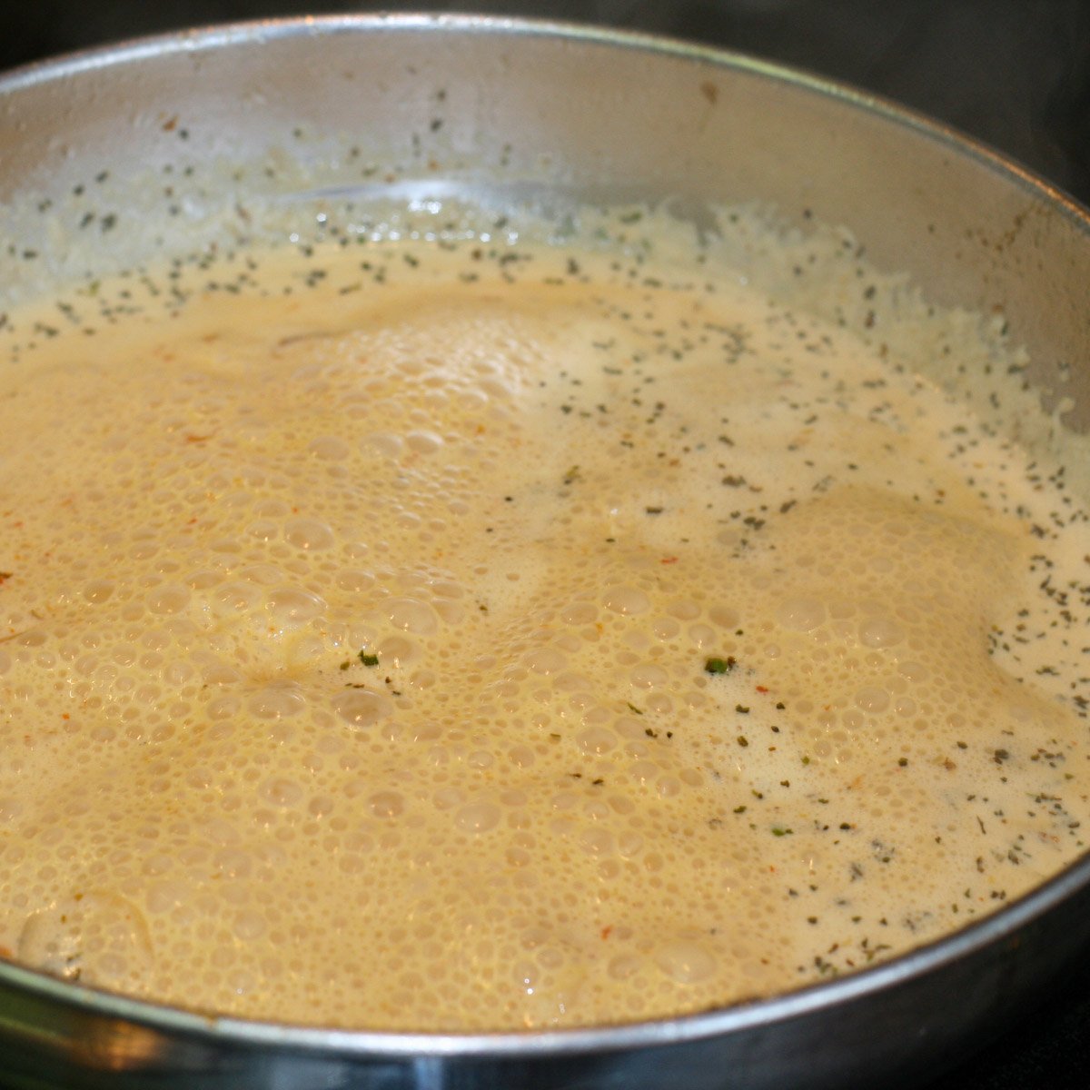 Sauce of sun-dried tomatoes, spices, white wine and cream simmering in skillet.