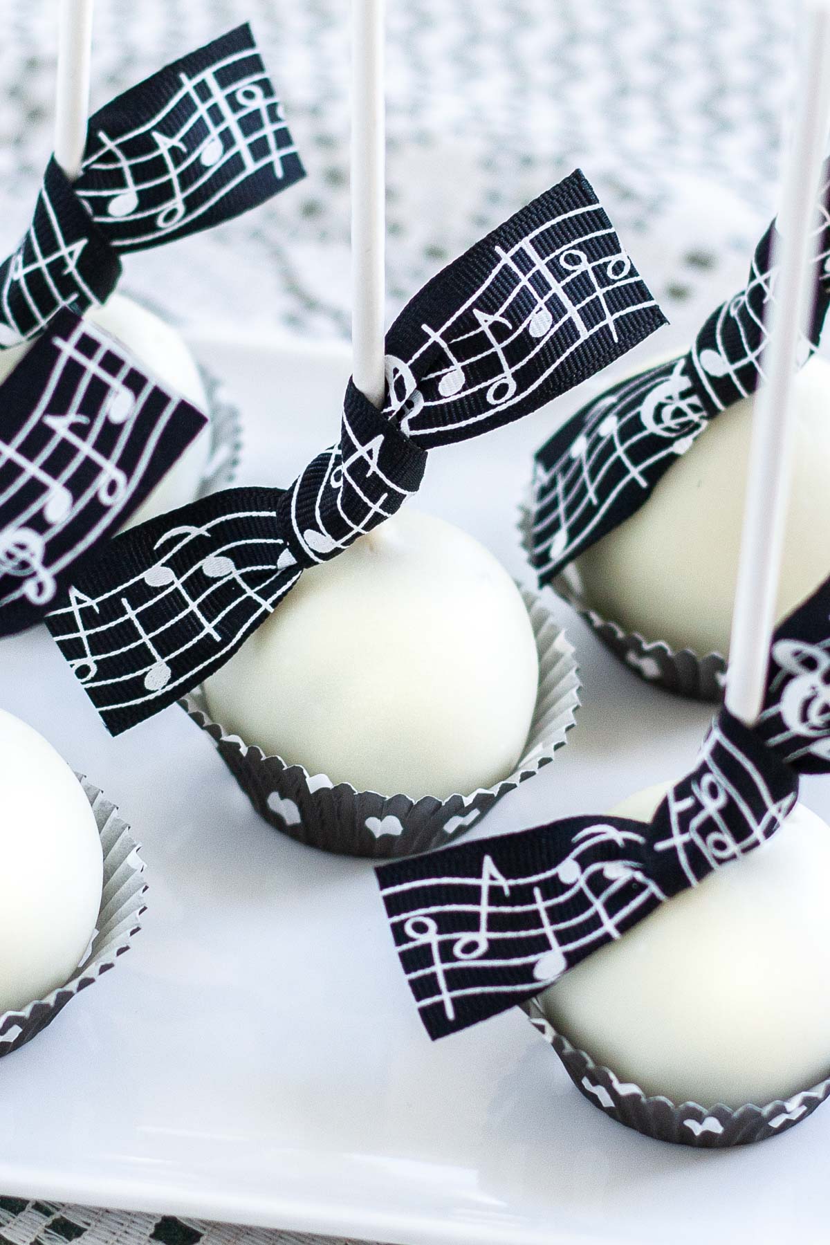 White chocolate coated cake pops with black music themed ribbon tied around the lollipop stick.