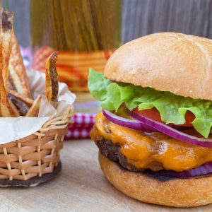 Homemade cheeseburger with slices of red onion, tomato and lettuce. Side of fries and glass of beer.