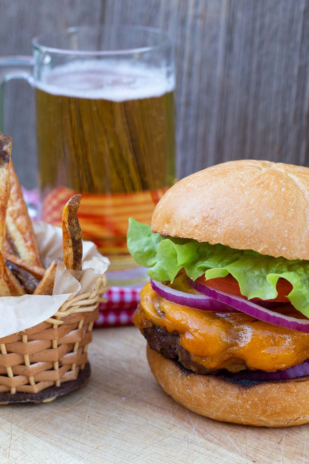 Homemade cheeseburger with slices of red onion, tomato and lettuce. Side of fries and glass of beer.