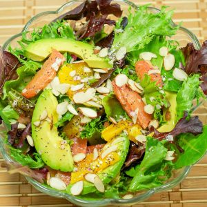 A bowl of fresh salad greens with avocado, grapefruit, and oranges. Sprinkled with almond slivers and poppyseed dressing.