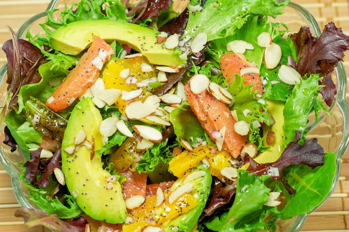 A bowl of fresh salad greens with avocado, grapefruit, and oranges. Sprinkled with almond slivers and poppyseed dressing.